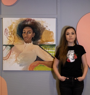 Taiteilija Anna Semerdjiev seisoo maalauksen vieressä, maalaus kuvaa tummaihoista naishenkilöä jossa on afrotukka. Konstrundan, Taiteen perjantai