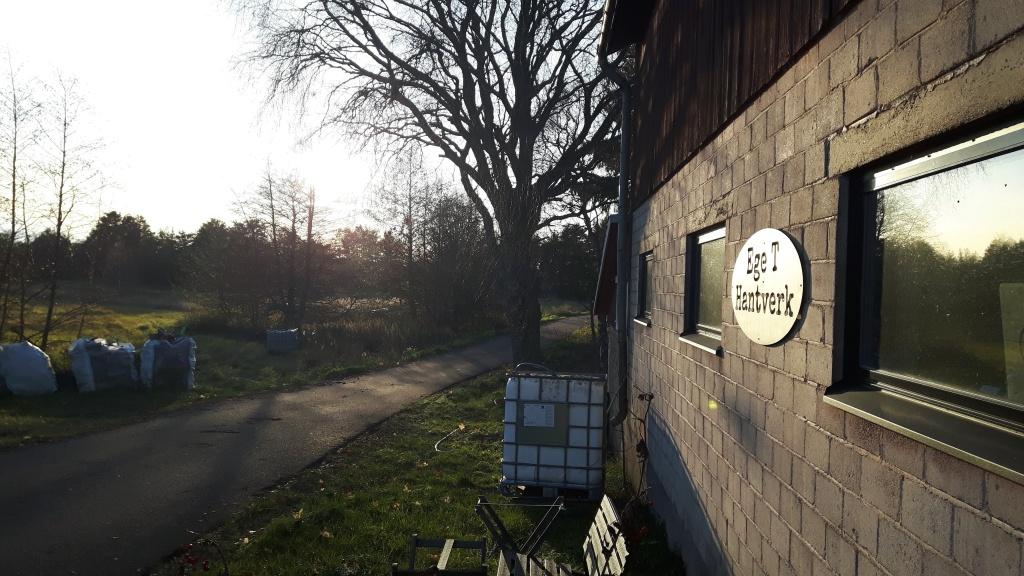 En gammal byggad av sten, ett träd och en väg. Konstrundan 2022