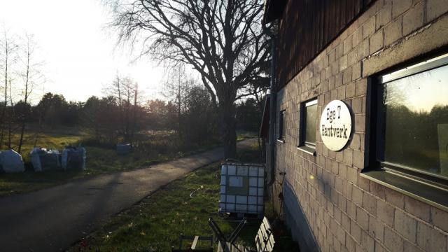 En gammal byggad av sten, ett träd och en väg. Konstrundan 2022
