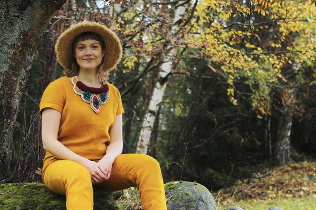 Alexandra Lindqvist, person in a yellow outfit sittning on a stone, smiling