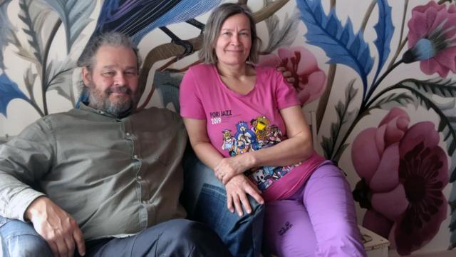 Pasi ja Virpi istuvat sohvalla hymyillen.