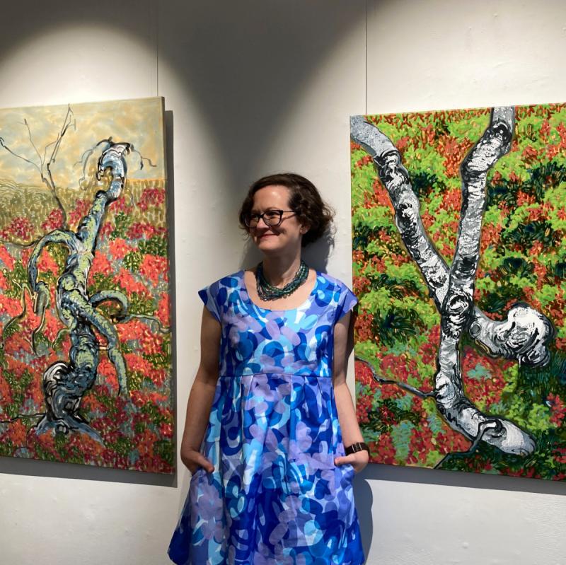 Petra Kaminen Mosher, artist standing between two of her paintings, 2023, Petra Kaminen Mosher